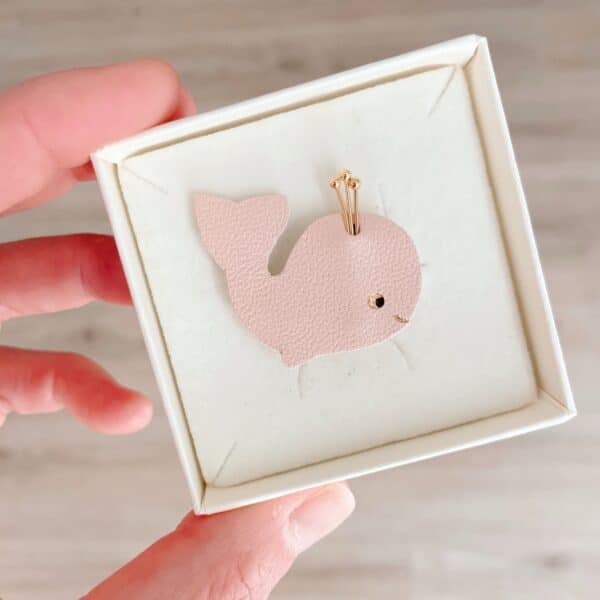 Broche baleine en cuir surcyclé rose poudré, détails dorés, tenue en main dans son écrin
