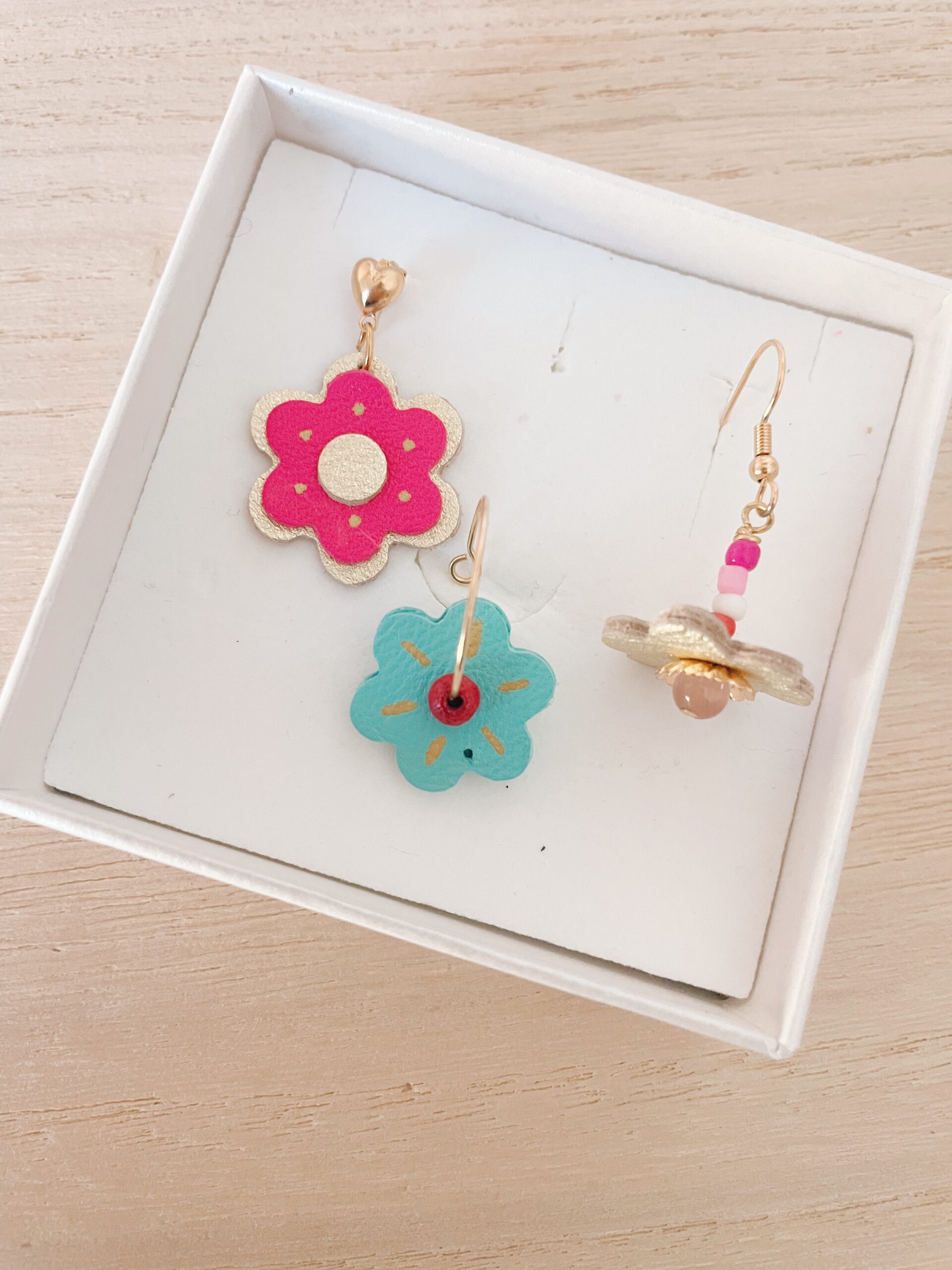 Créations enfants – boucles d'oreilles fleurs en cuir doré | Atelier anniversaire Du vent dans mes valises Légende (optionnelle, très utile ici) : Boucles d'oreilles fleurs en cuir coloré réalisées par des enfants lors d'un atelier créatif anniversaire – rose fuchsia, bleu turquoise et doré, Côte d'Opale