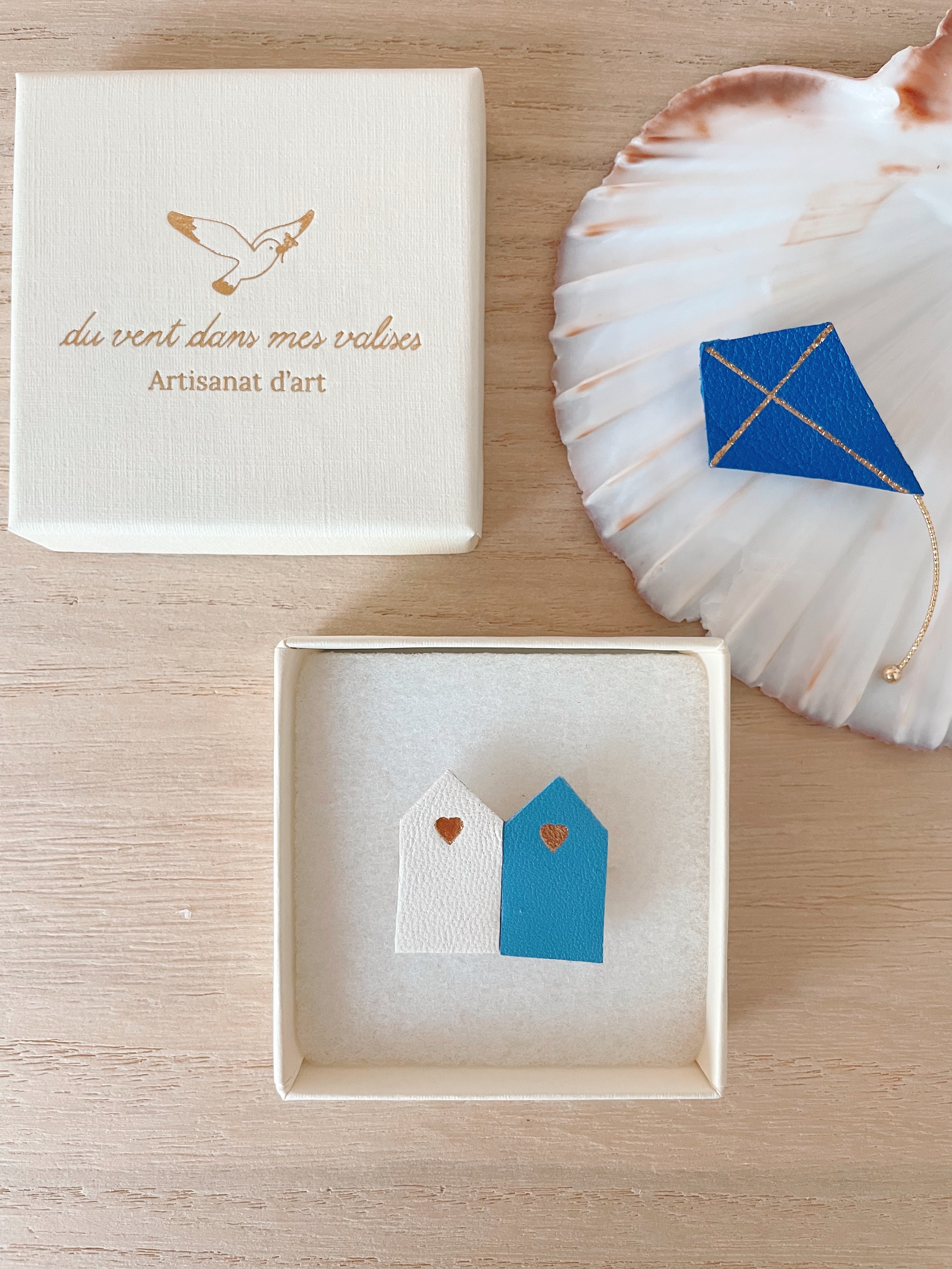 Broche cabines de plage Bleu Wimereux — écrin et cerf-volant © Du vent dans mes valises Broche duo cabines de plage Bleu Wimereux en cuir surcyclé dans son écrin, broche cerf-volant bleu sur coquille en arrière-plan