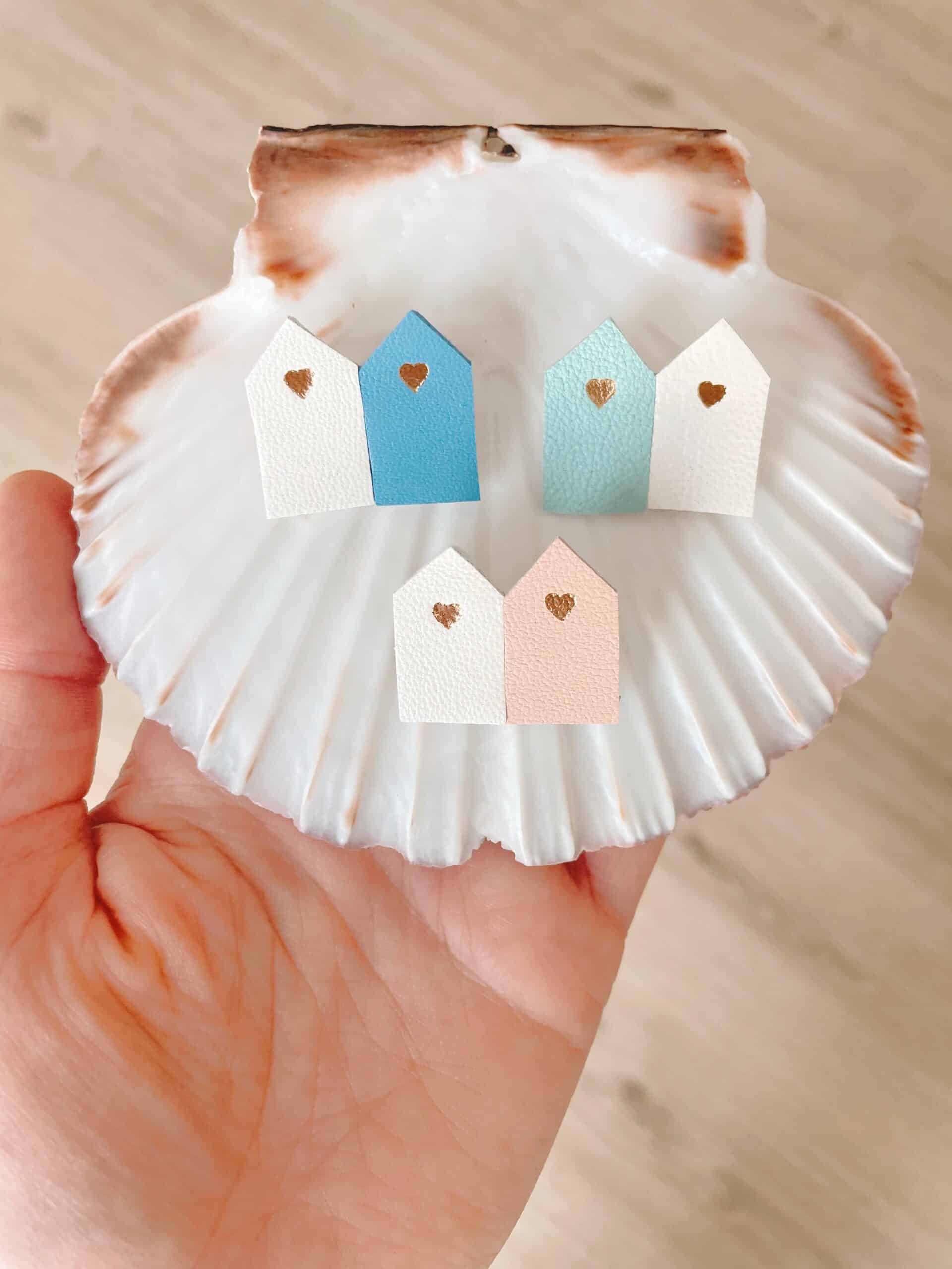 Broches cabines de plage cuir sur coquille — vue en plongée © Du vent dans mes valises Broches duo cabines de plage en cuir surcyclé sur grande coquille naturelle tenue en main, vue en plongée