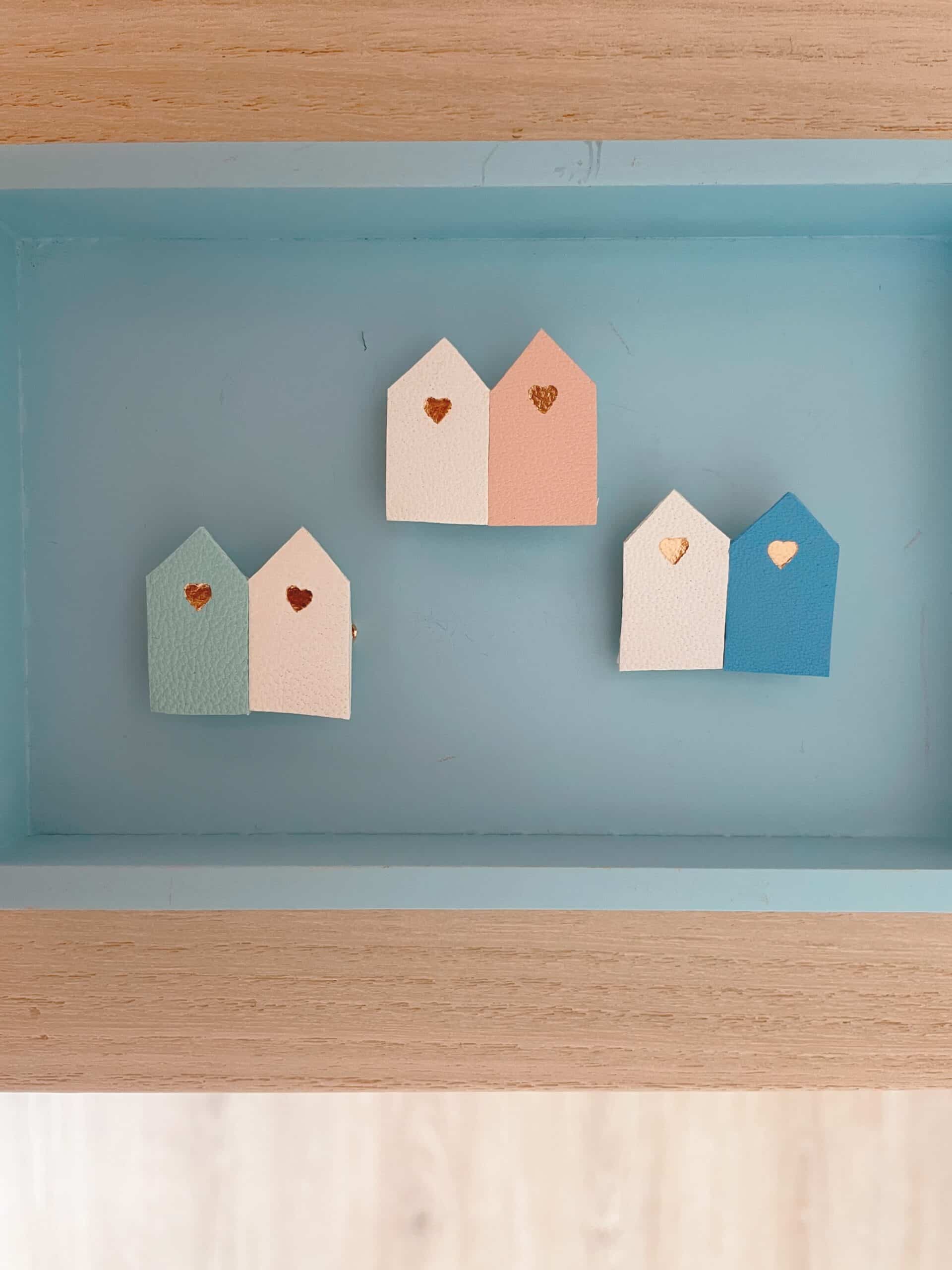 Broches duo cabines de plage cuir — cadre bleu vue dessus © Du vent dans mes valises Trois broches duo cabines de plage en cuir surcyclé dans un cadre bleu, vue de dessus, tous coloris visibles