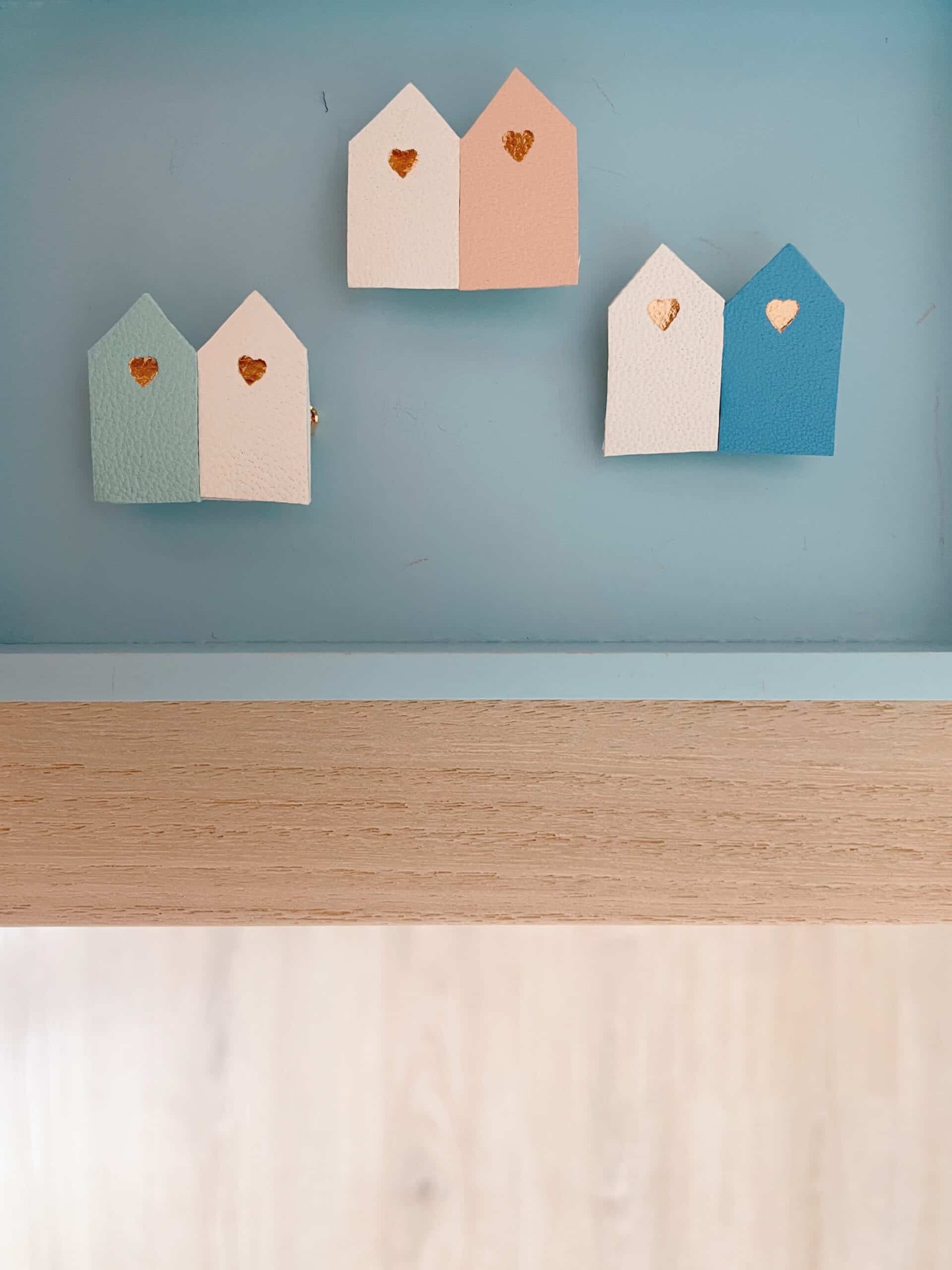 Broches duo cabines de plage cuir — fond bleu © Du vent dans mes valises Trois broches duo cabines de plage en cuir surcyclé épinglées sur fond bleu, cœurs dorés visibles
