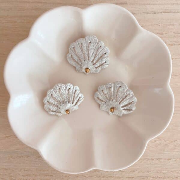 Trois broches coquille Saint-Jacques en cuir surcyclé argenté posées dans une coupelle blanche