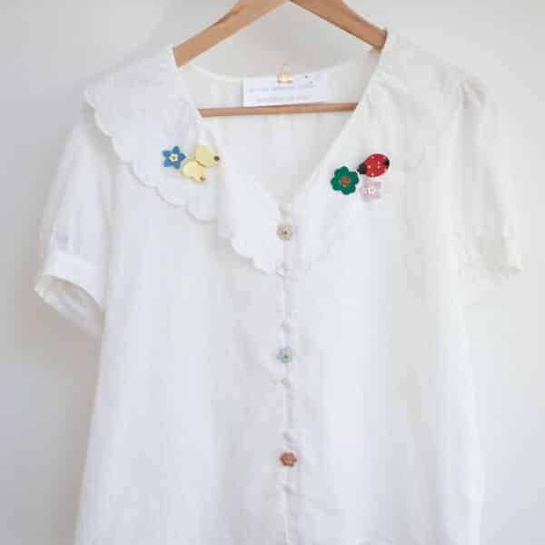 Collection de broches en cuir colorées épinglées sur une blouse blanche en lin — papillon jaune, coccinelle rouge, myosotis bleu et rose, trèfle, artisanat d'art Du Vent dans mes Valises