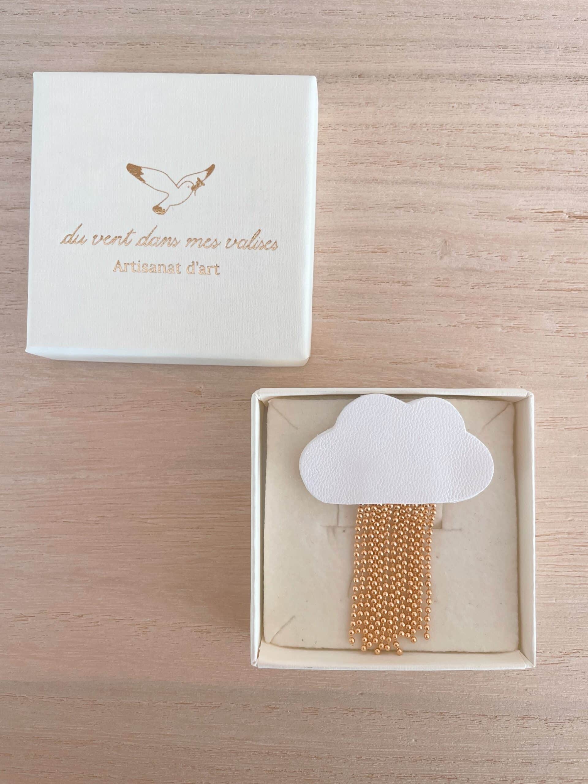 Broche nuage L'Ondée — écrin prête à offrir © Du vent dans mes valises Broche nuage L'Ondée en cuir blanc dans son écrin ouvert, boîte Du vent dans mes valises à côté, sur bois