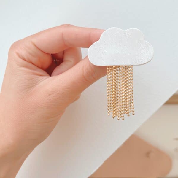 Broche nuage L'Ondée en cuir surcyclé blanc tenue en main, pluie de chaînes dorées déployée, fond blanc