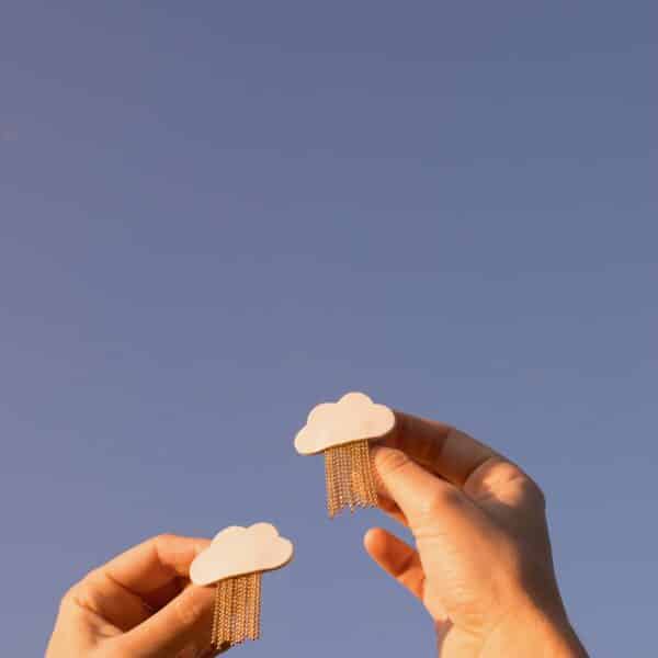 Deux broches nuage L'Ondée en cuir surcyclé blanc, pluie de chaînes dorées, tendues vers un ciel bleu