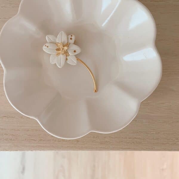 Broche edelweiss en cuir blanc, points dorés et tige dorée, posée dans une coupelle en porcelaine festonnée
