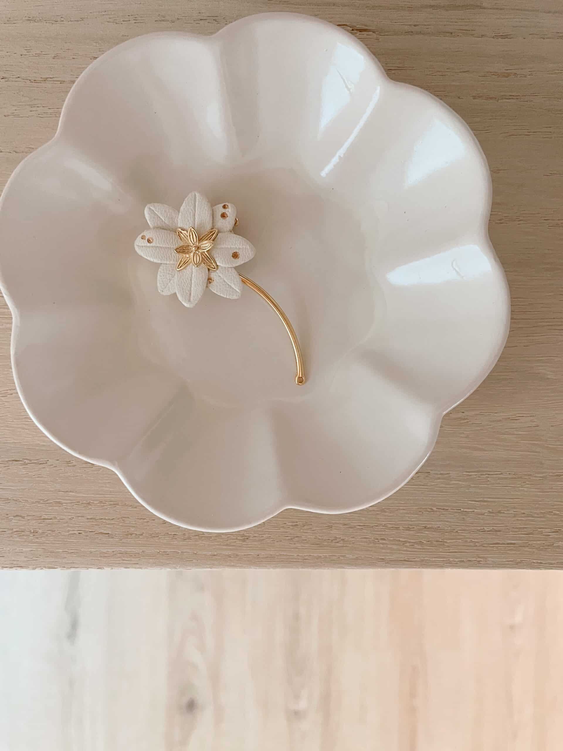 Broche edelweiss en cuir blanc, points dorés et tige dorée, posée dans une coupelle en porcelaine festonnée