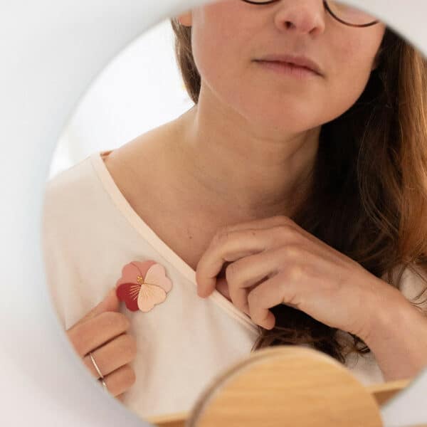 Femme épinglant une broche pensée d'amour en cuir bicolore rouge et rose sur un t-shirt blanc, reflet dans un miroir rond — Du Vent dans mes Valises