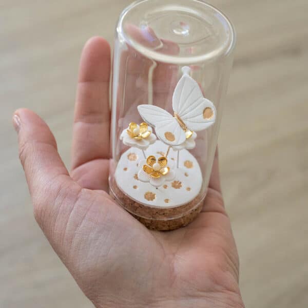 Jardin de poche papillon en cloche de verre tenu dans une main, univers miniature en cuir blanc et doré — objet poétique artisanat d'art Côte d'Opale Du Vent dans mes Valises