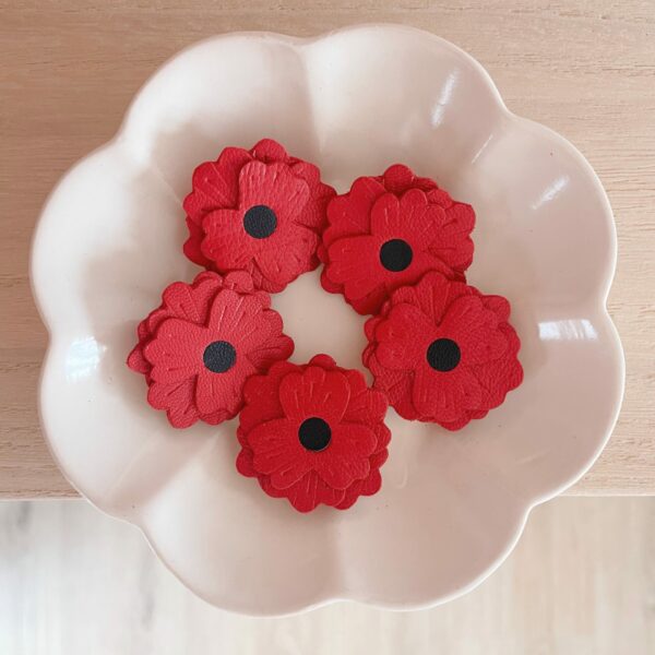 Cinq broches coquelicot en cuir surcyclé rouge, cœur noir, disposées dans une coupelle blanche vue de dessus