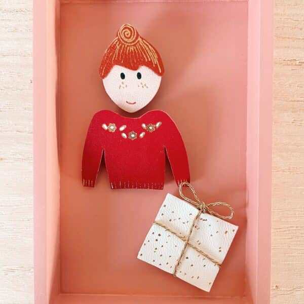 Broche en cuir représentant un visage stylisé avec un chignon et des détails dorés sur les pommettes, pièce unique et personnalisable.