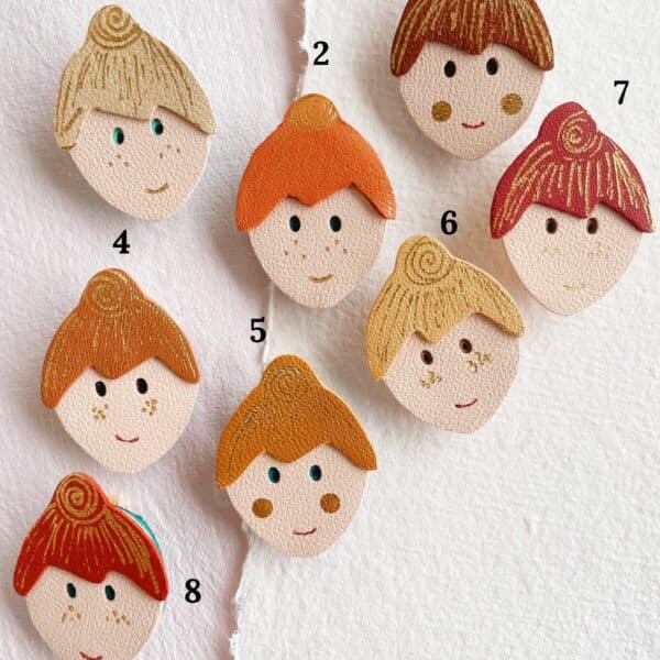 Broche en cuir représentant un visage stylisé avec un chignon et des détails dorés sur les pommettes, pièce unique et personnalisable.