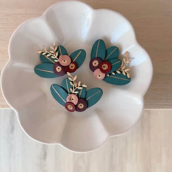 Broches baies en cuir surcyclé dans une coupelle, baies rose, bordeaux et prune sur feuilles vert sapin dorées à l'or fin
