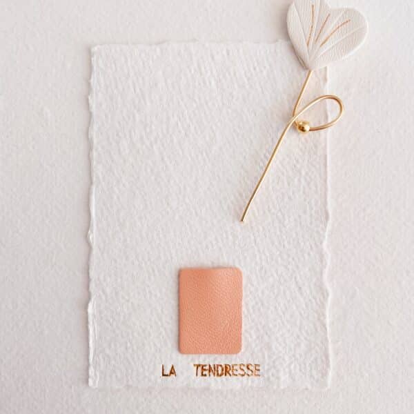 Fleur d’Amour posée sur carte artisanale La Tendresse, en cuir ivoire avec dorure or fin