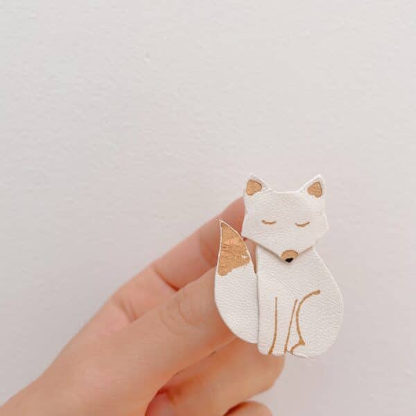 Broche renard blanche dorée tenue entre les doigts, vue d’échelle