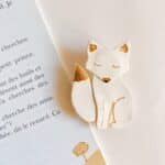 Broche renard blanche avec détails dorés posée sur une page de livre