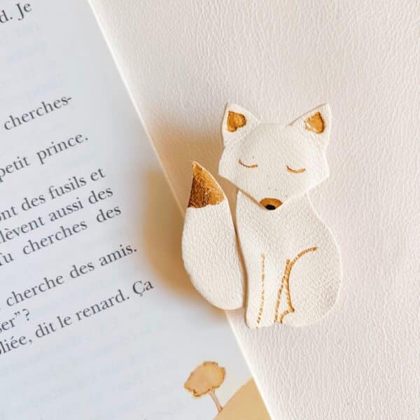Broche renard blanche avec détails dorés posée sur une page de livre