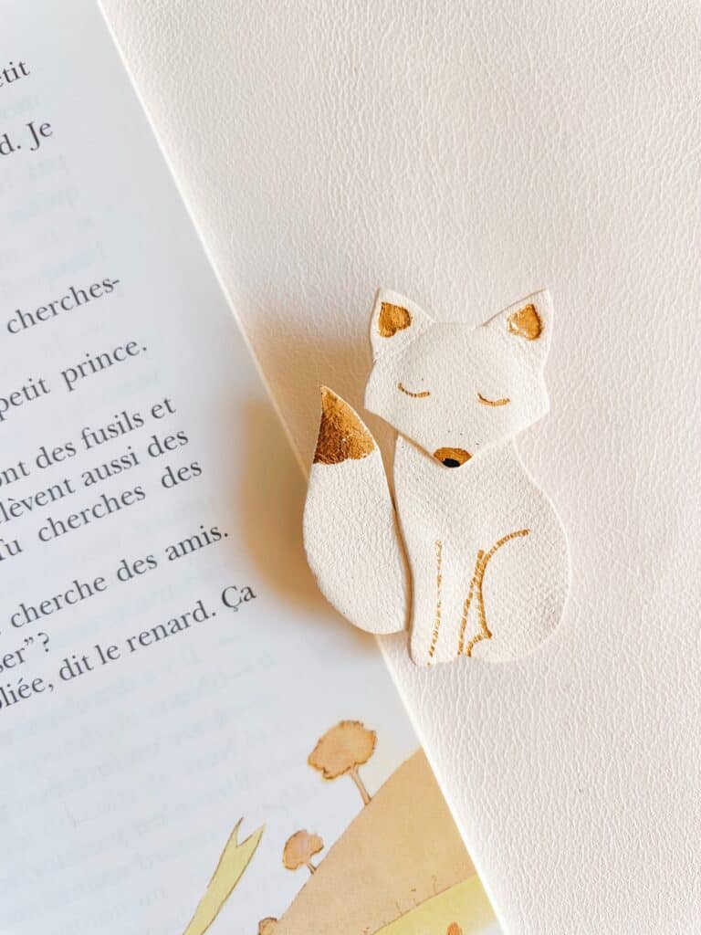Broche renard blanche avec détails dorés posée sur une page de livre