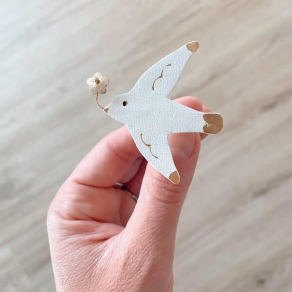Broche mouette heureuse en cuir surcyclé blanc tenue en main, petite fleur dorée au bec