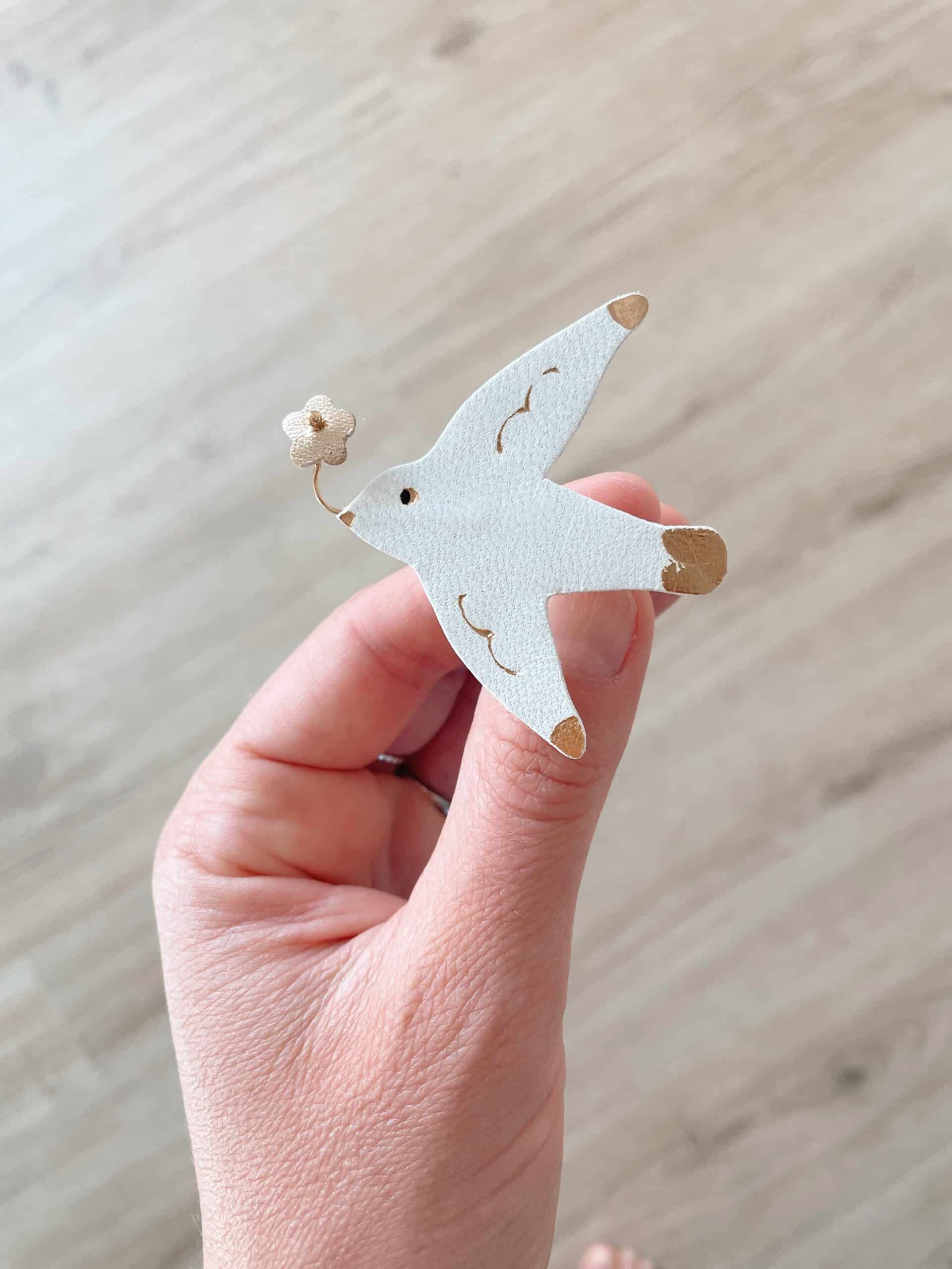 Broche mouette heureuse cuir blanc tenue en main © Du vent dans mes valises Broche mouette heureuse en cuir surcyclé blanc tenue en main, petite fleur dorée au bec