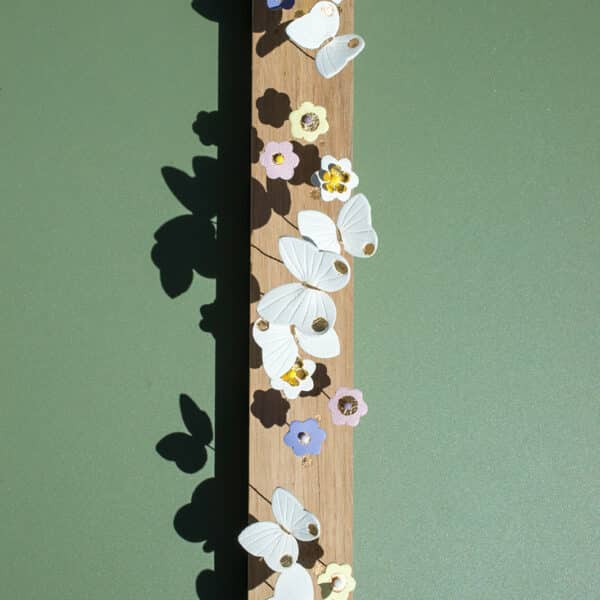 Jardin de table en cuir surcyclé — papillons blancs et fleurs colorées épinglés sur une planche en bois, ombres portées sur fond vert