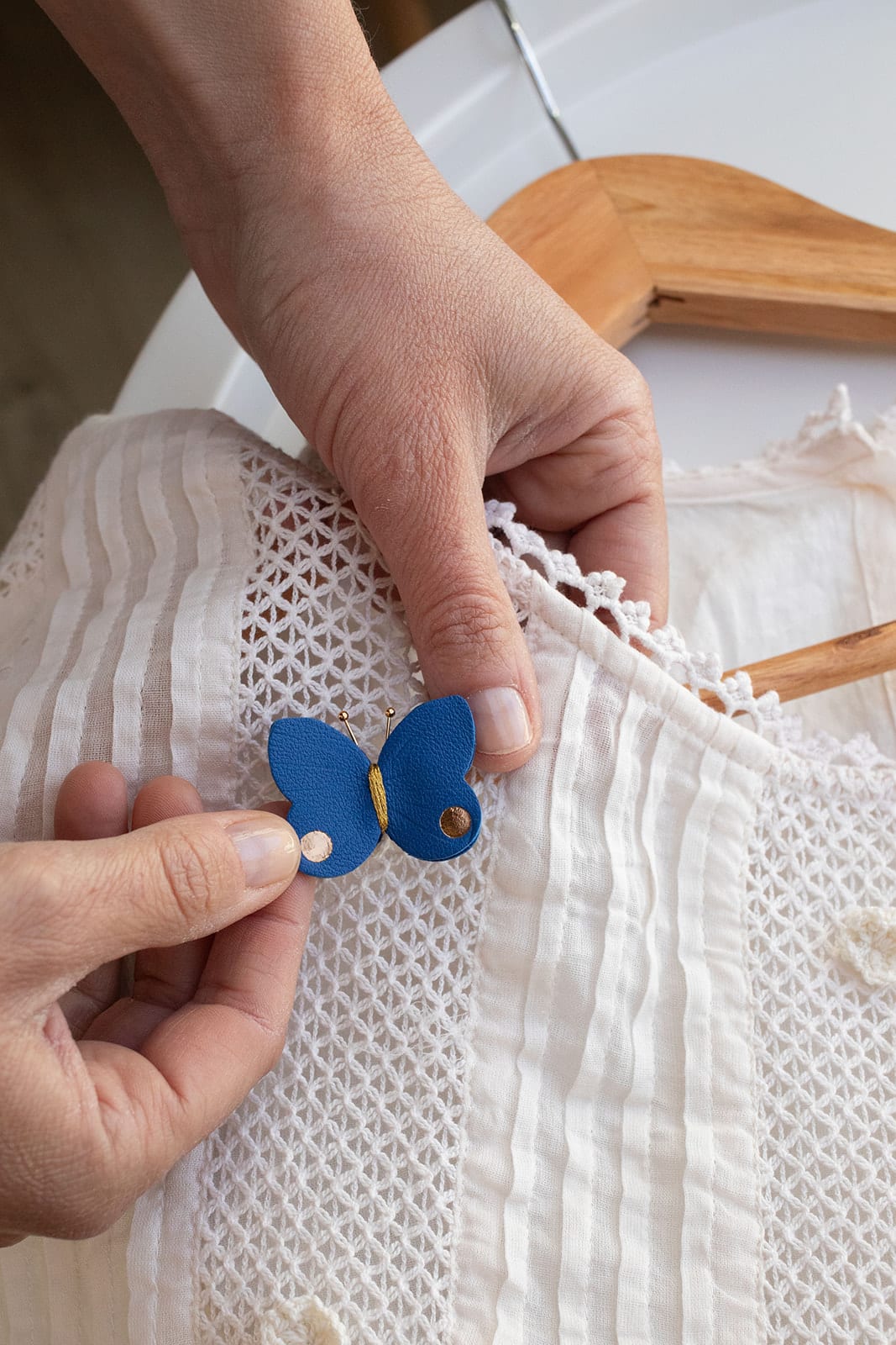Broche papillon cuir bleu cobalt tenue en main © Du vent dans mes valises papillon-cuir-bleu-cobalt-dore-tenue-main-du-vent-dans-mes-valises.jpg Alt : Broche papillon en cuir surcyclé bleu cobalt et détails dorés tenue en main sur tissu blanc brodé