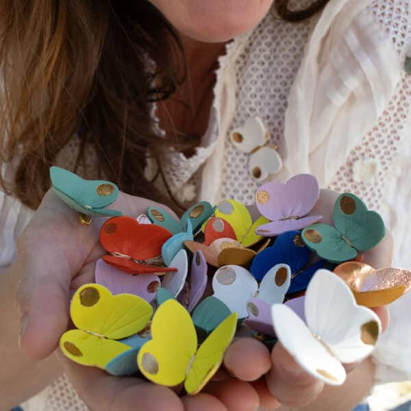 Nuée de petits papillons en cuir surcyclé multicolores tenus dans les deux mains