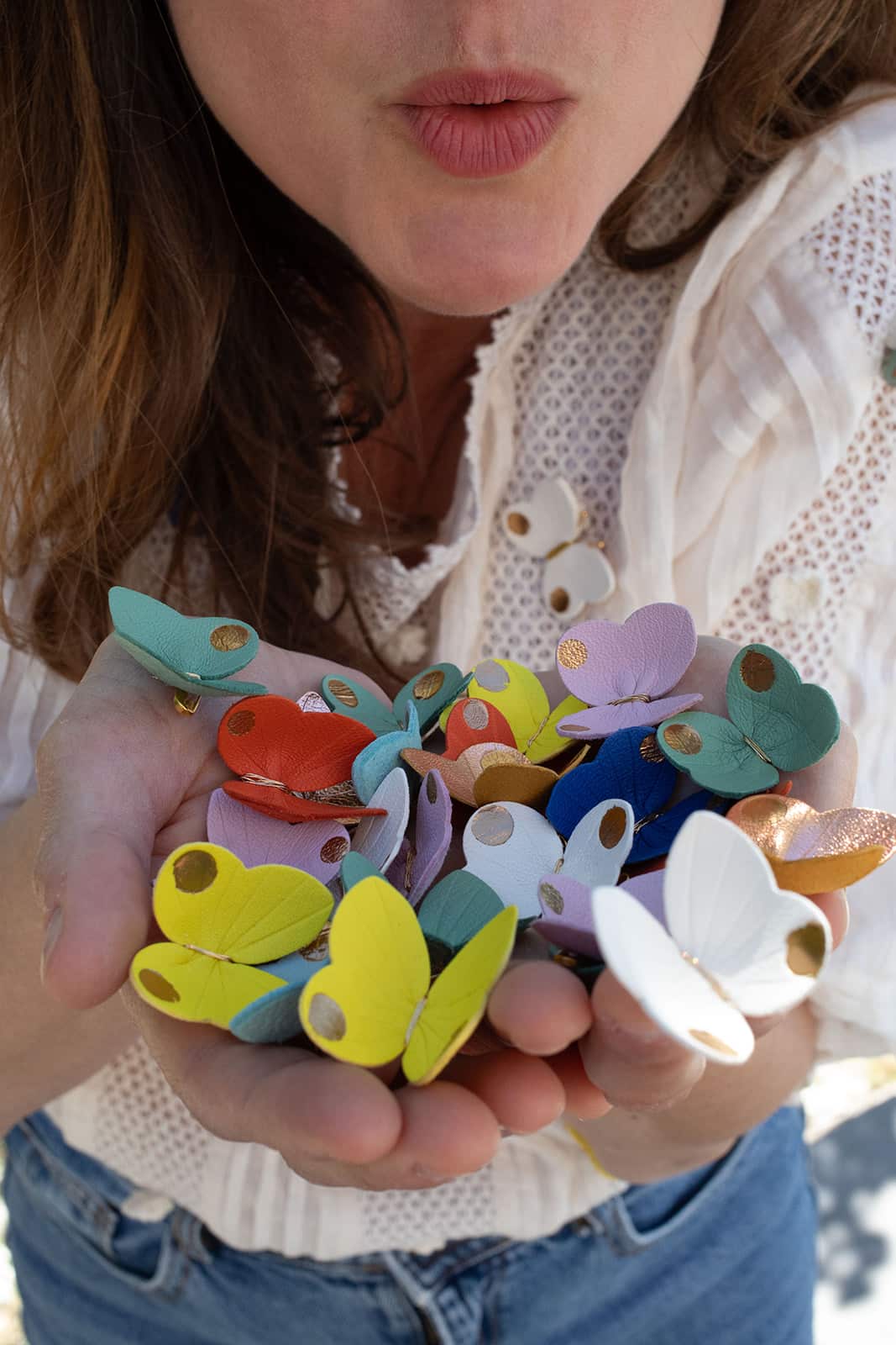 Nuée de petits papillons en cuir surcyclé multicolores tenus dans les deux mains
