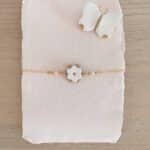 Bracelet Corolles fleur ivoire et or, détails quartz rose facetté, présenté sur papier artisanat rosé avec broche papillon