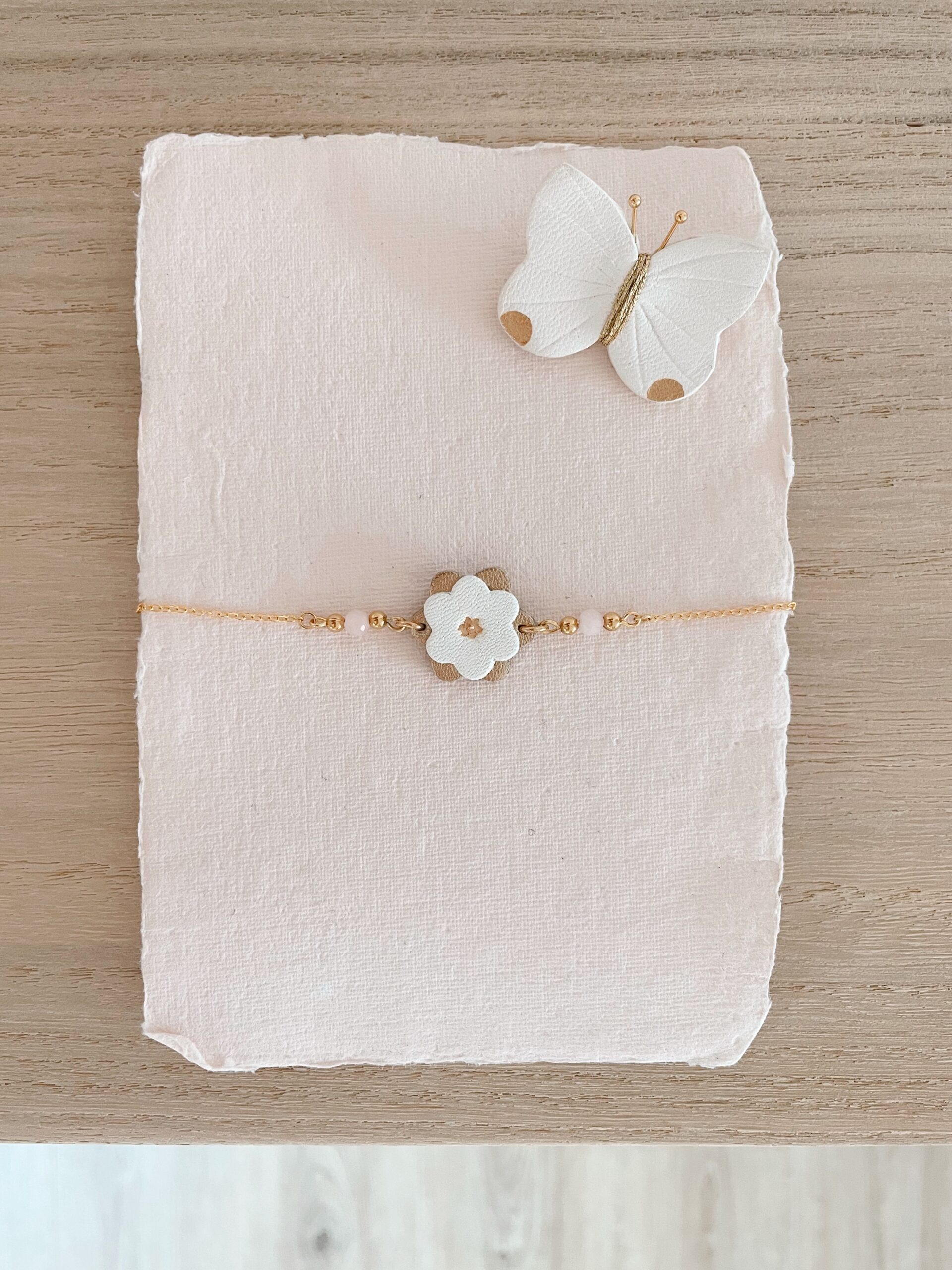 Bracelet Corolles fleur ivoire et or, détails quartz rose facetté, présenté sur papier artisanat rosé avec broche papillon