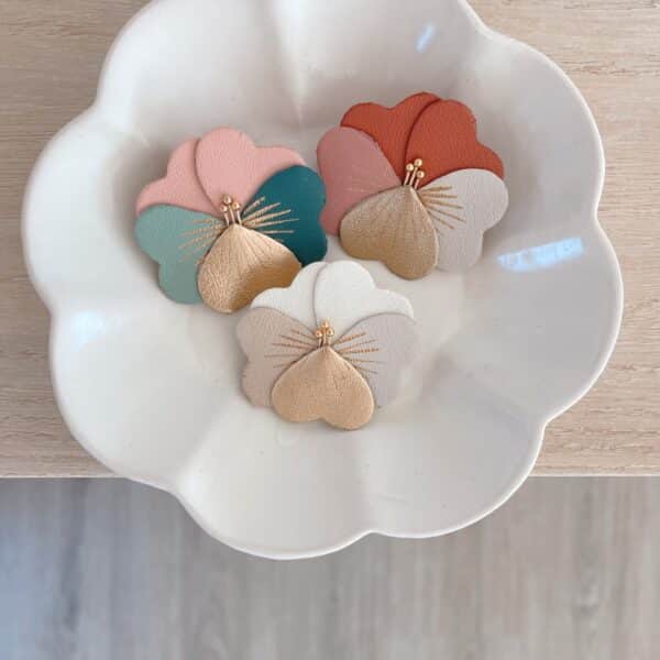 Trio de broches pensées bucoliques sur coupelle blanche : tons crème, verts poudrés et terre cuite, détails dorés.