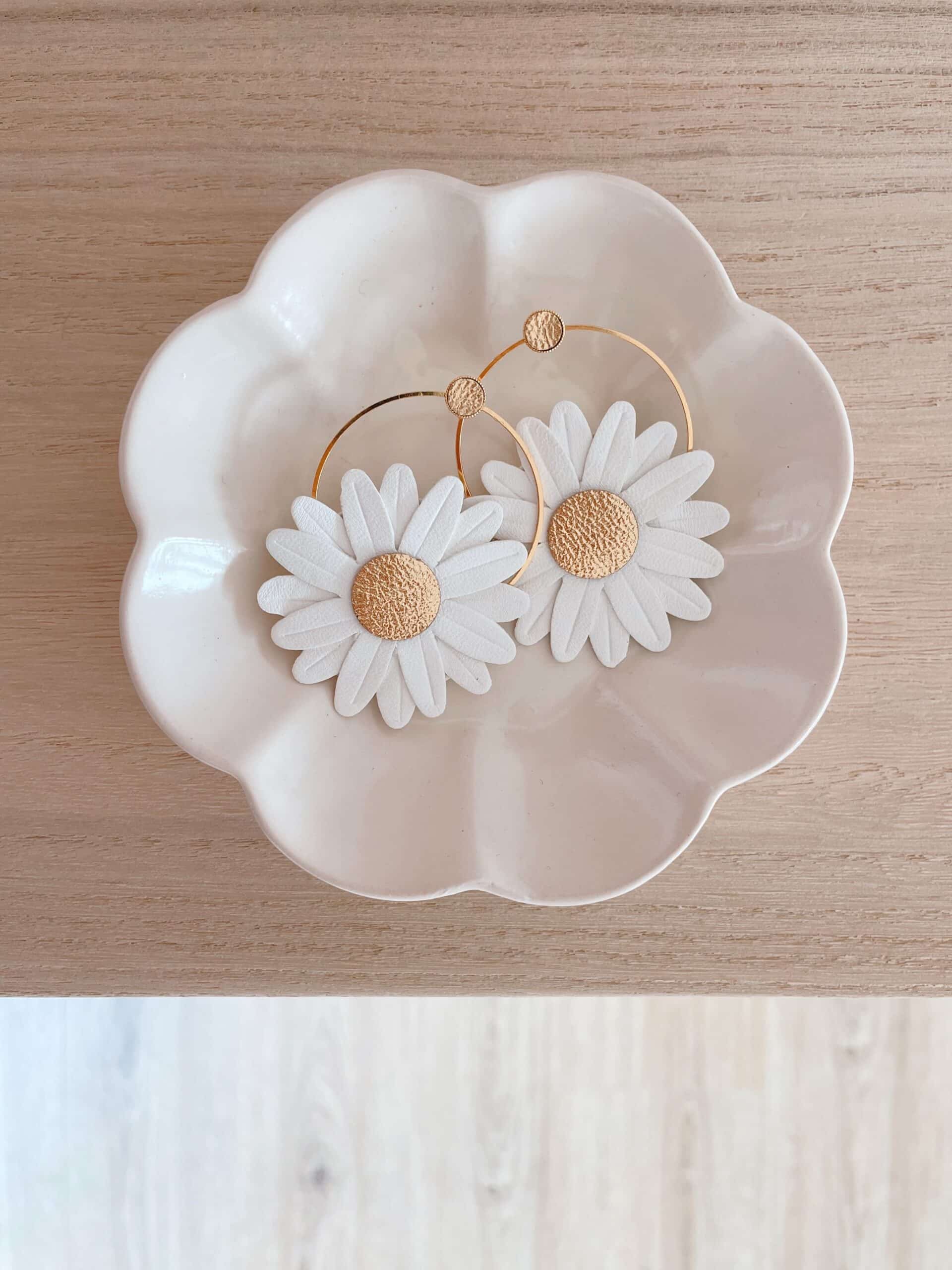 Boucles d’oreilles Marguerite créoles blanches cœur doré © Du vent dans mes valises Boucles d’oreilles Marguerite blanches cœur doré en créoles, posées dans une coupelle