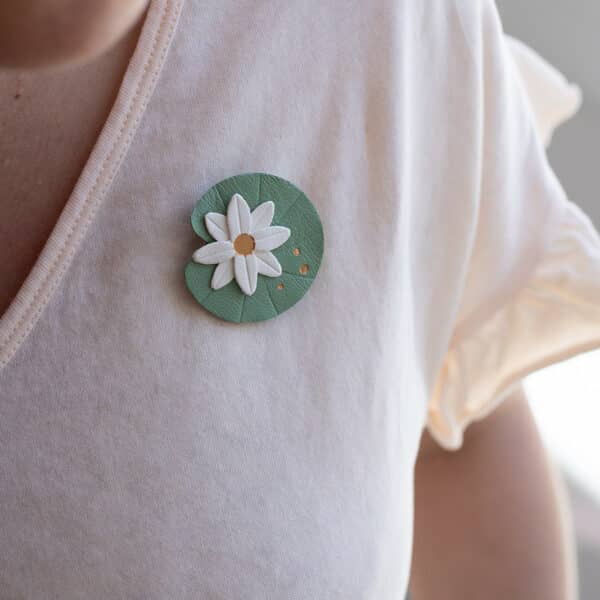 Broche Nymphéa nénuphar en cuir blanc sur fond rond vert gravé avec dorure à chaud à l'or fin, portée sur t-shirt ivoire — Du Vent dans mes Valises