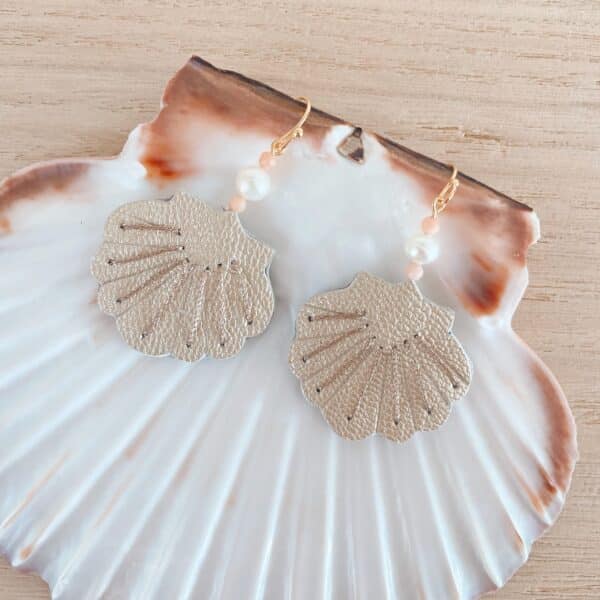 Boucles d'oreilles coquille en cuir nacré argenté posées sur une grande coquille naturelle, perle et quartz roses