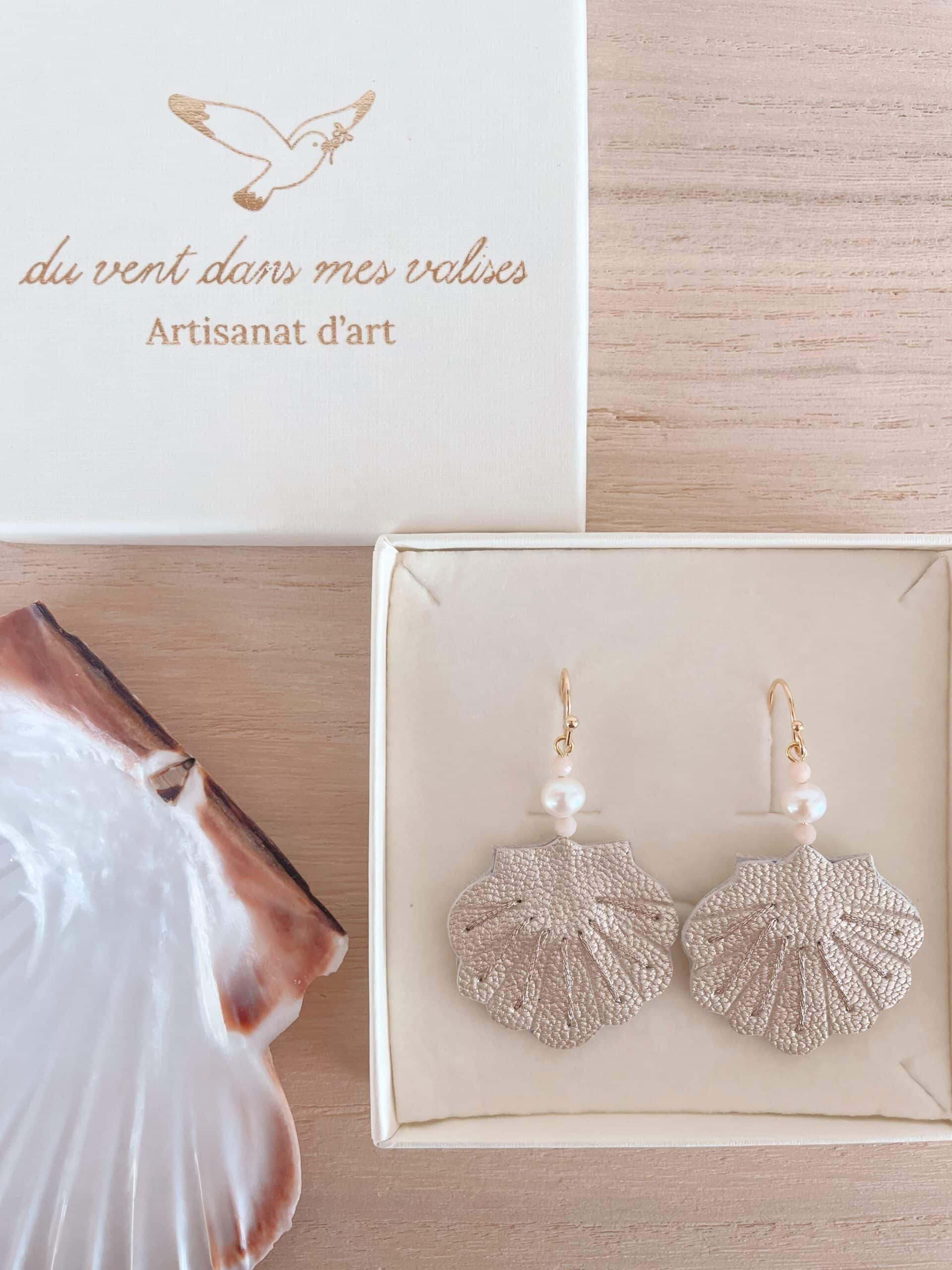 Boucles d'oreilles coquille cuir nacré — écrin prêtes à offrir © Du vent dans mes valises Boucles d'oreilles coquille en cuir nacré dans leur écrin ouvert, boîte Du vent dans mes valises et coquille naturelle en arrière-plan