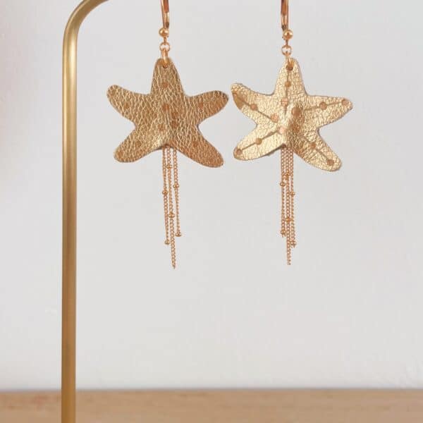 Paire de boucles d'oreilles étoile de mer en cuir surcyclé doré, dorure à chaud, chaînes de laiton dorées, sur présentoir