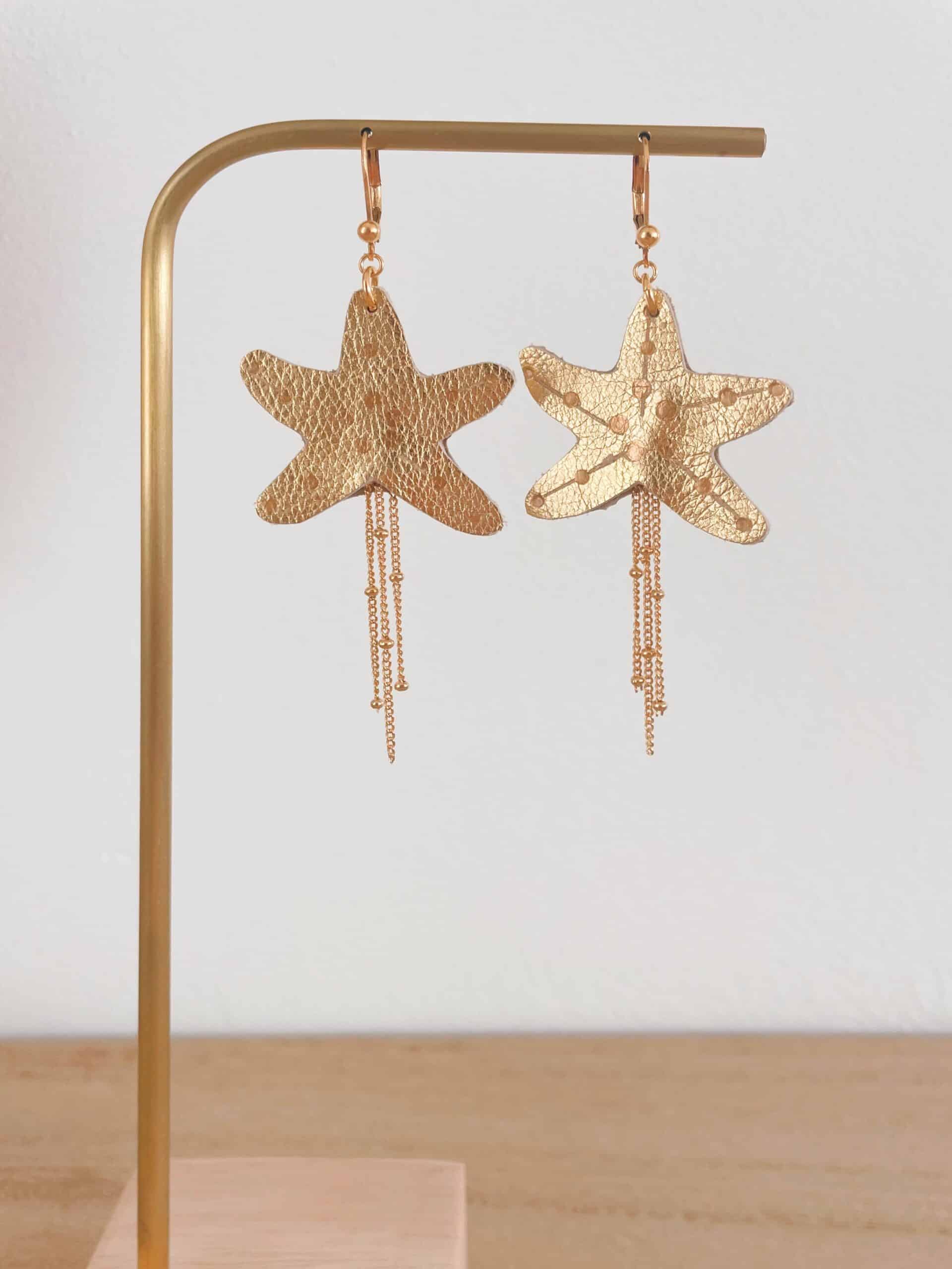 Paire de boucles d'oreilles étoile de mer en cuir surcyclé doré, dorure à chaud, chaînes de laiton dorées, sur présentoir
