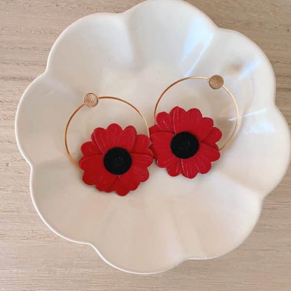 Paire de boucles d'oreilles coquelicot en cuir surcyclé rouge, cœur noir, sur créoles dorées, posées dans une coupelle blanche