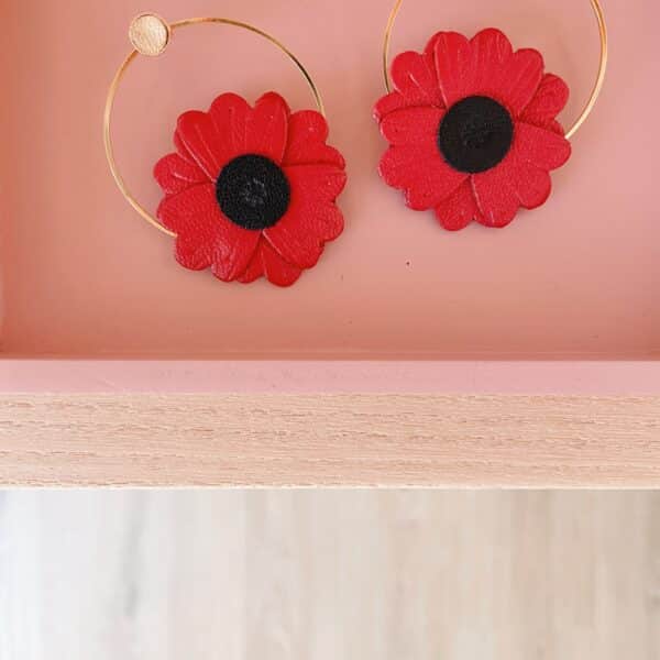 Paire de boucles d'oreilles coquelicot en cuir rouge et créoles dorées posées dans un cadre rose