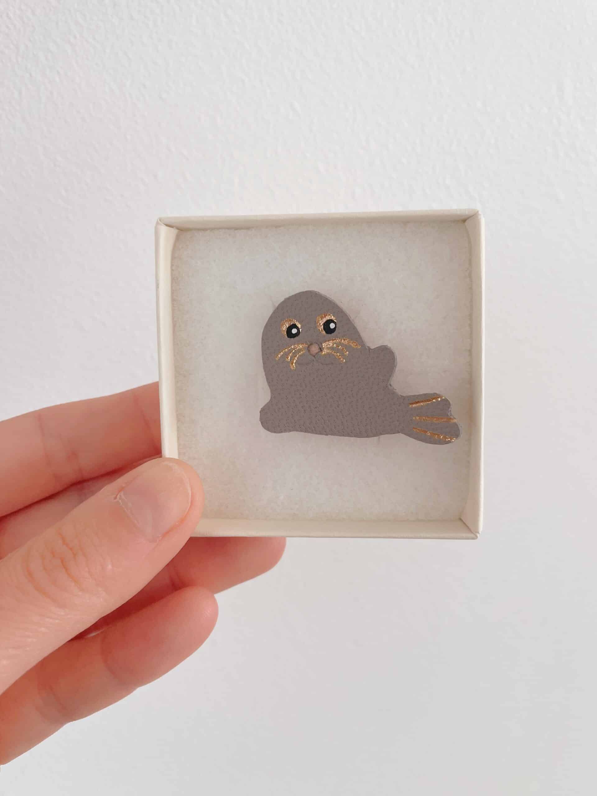 Broche phoque Selkie gris bleuté — écrin © Du vent dans mes valises Broche phoque Selkie en cuir surcyclé gris bleuté tenue en main dans son écrin