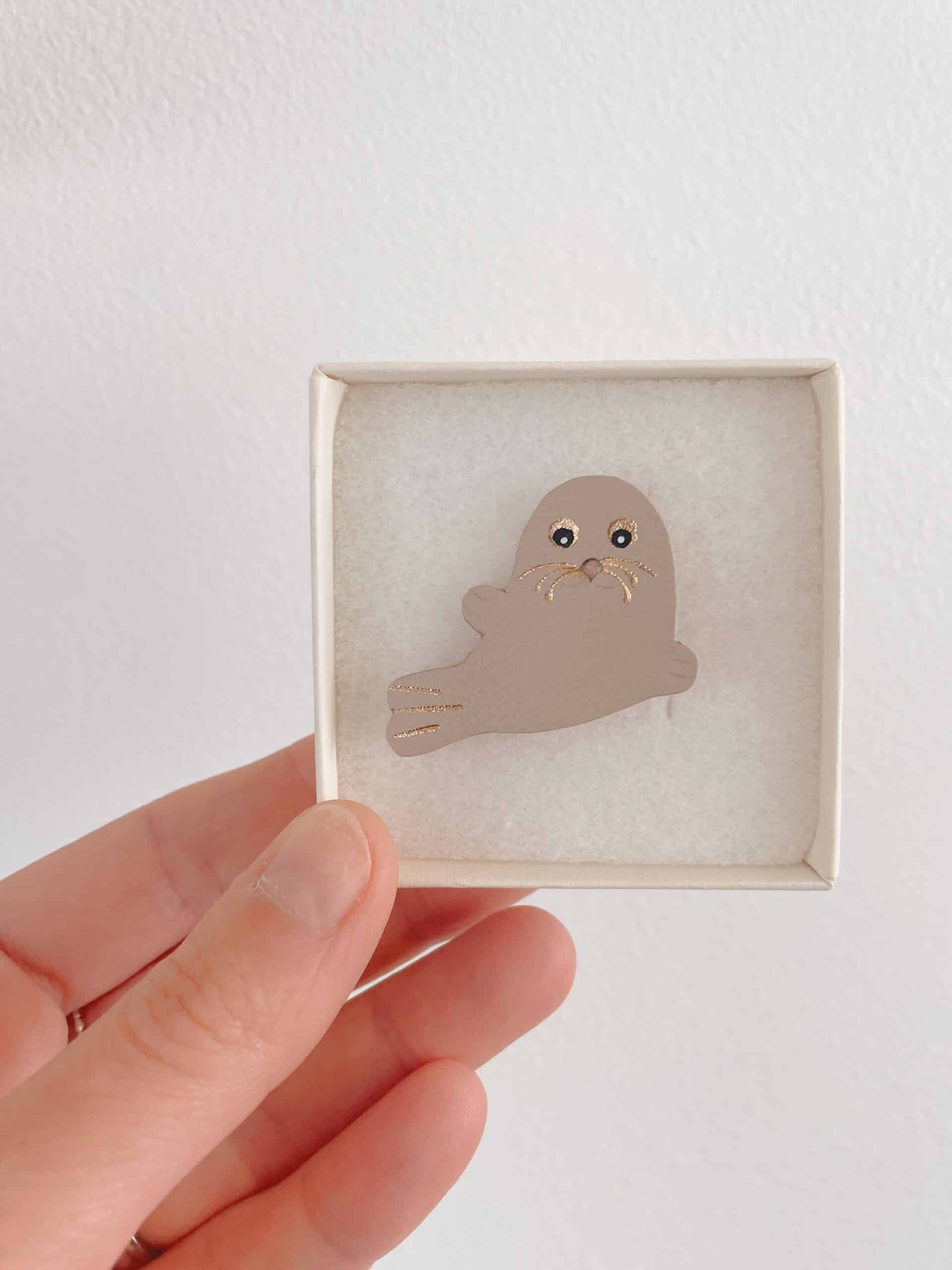 Broche phoque Selkie beige rosé — écrin © Du vent dans mes valises Broche phoque Selkie en cuir surcyclé beige rosé tenue en main dans son écrin