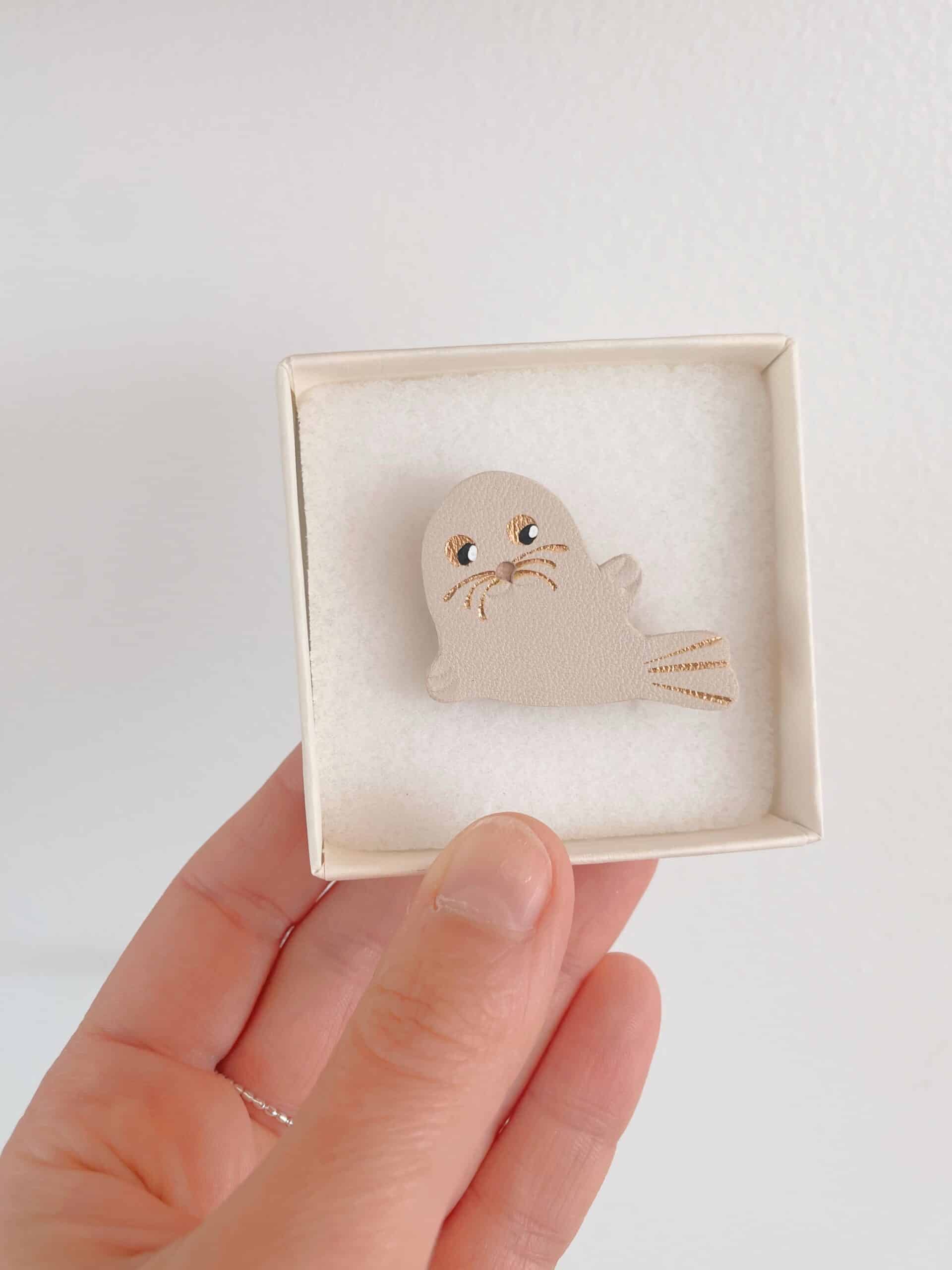 Broche phoque Selkie blanc cassé — écrin © Du vent dans mes valises Broche phoque Selkie en cuir surcyclé blanc cassé tenue en main dans son écrin