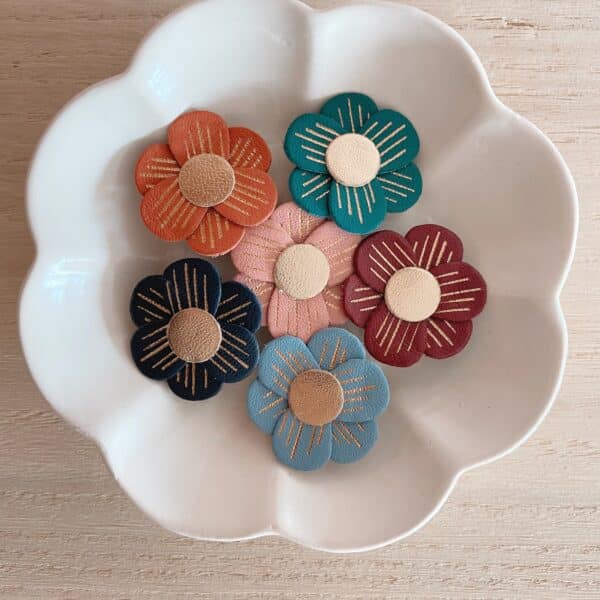 Six broches Lison en cuir surcyclé aux coloris d'automne-hiver — rose ancien, bordeaux, sapin, bleu nuit, bleu gris et rouille — dans une coupelle blanche