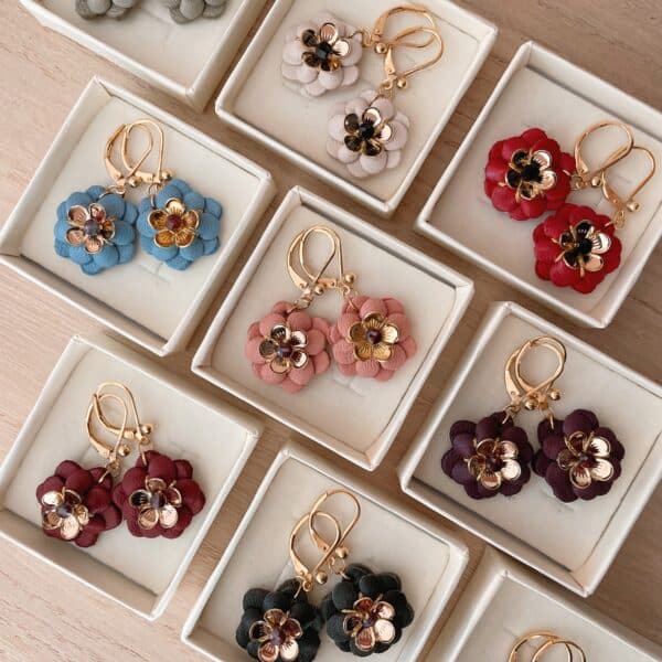 Neuf paires de boucles d’oreilles fleurs en cuir coloré, cœur doré et pierre facettée, présentées dans des écrins crème