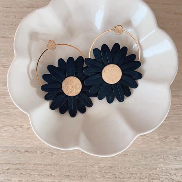 Paire de boucles d’oreilles marguerite en cuir surcyclé bleu nuit, cœur doré, sur créoles dorées, dans une coupelle blanche