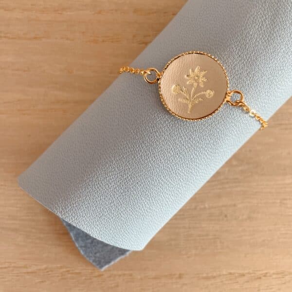 Bracelet médaillon edelweiss en cuir doré enroulé autour d’un rouleau de cuir gris-bleu